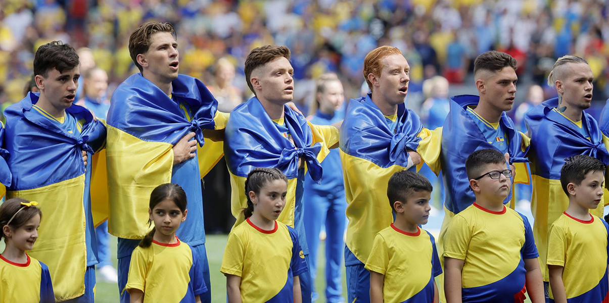 Los jugadores ucranianos, arropados por la bandera de su país a su salida al campo